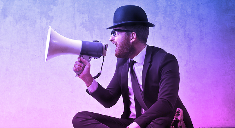 Man with hat on talking into loud speaker